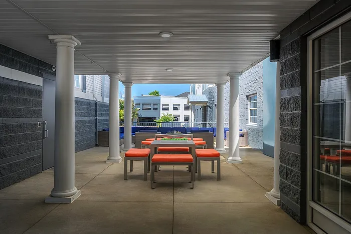 Chic outdoor patio featuring stylish orange-cushioned seating and elegant white columns, perfect for relaxation and gatherings.