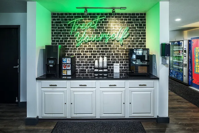 Chic coffee station with neon 'Treat Yourself' sign, featuring modern beverage dispensers and stylish cabinetry.