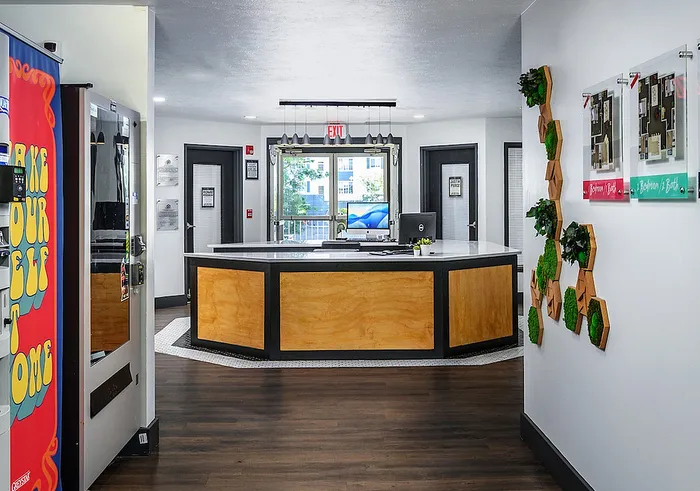 Modern apartment leasing office with stylish wooden desk, decorative wall art, and bright natural lighting.