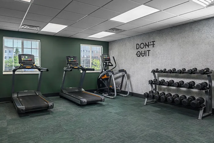 Modern on-site fitness center with treadmills, exercise bike, and free weights, featuring motivational 'Don't Quit' wall decor.