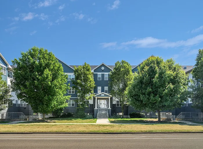 Charming residential building with classic architecture, surrounded by lush greenery and a clear blue sky backdrop.