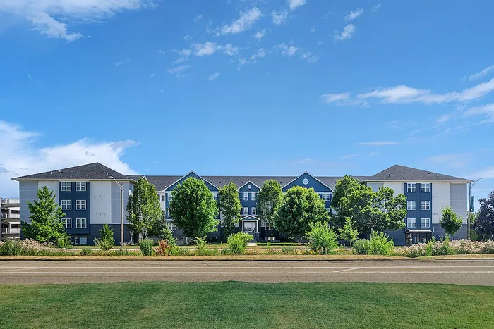 Charming apartment complex with a modern exterior, framed by lush greenery and a clear blue sky, promising serene living.