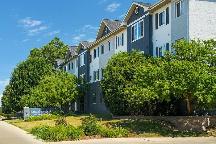Charming residential apartment building surrounded by lush greenery under a clear blue sky.