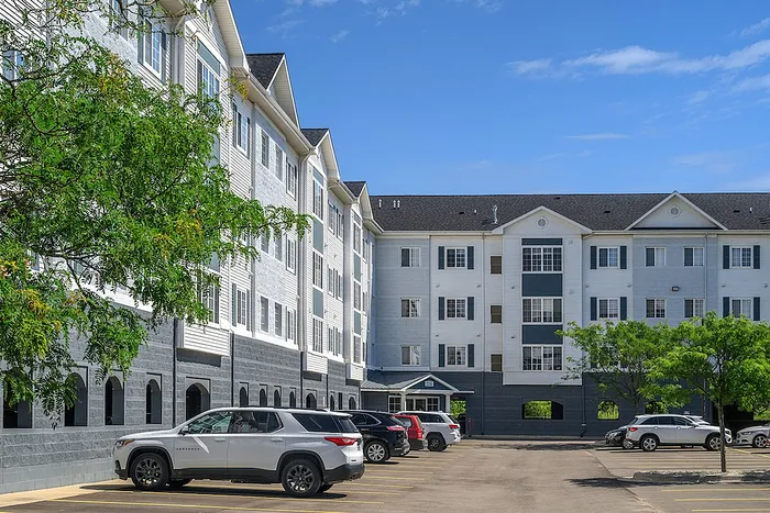 Modern apartment building with elegant facade, ample parking, and lush greenery under a clear blue sky.