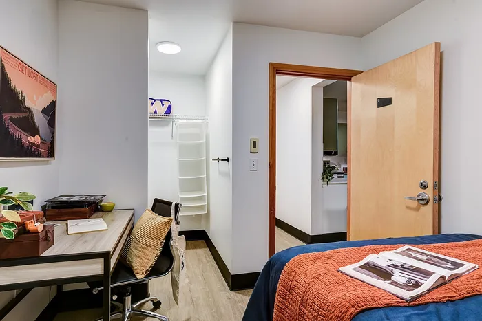 Cozy bedroom with inviting study nook and open closet space, featuring a modern design and warm wooden accents.