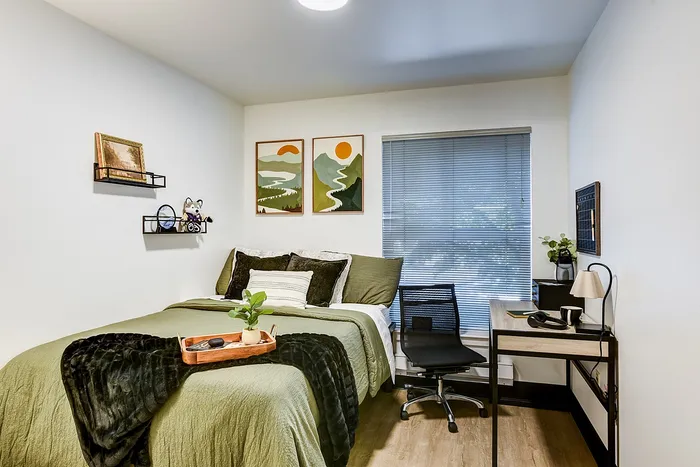 Cozy bedroom with a modern desk setup, stylish wall art, and natural light filtering through blinds.