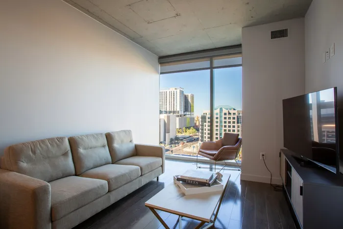 Modern living room featuring a plush sofa, sleek TV setup, and floor-to-ceiling windows offering stunning urban views.
