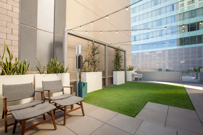 Chic urban patio with cozy lounge chairs, lush greenery, and twinkling string lights in a modern setting.