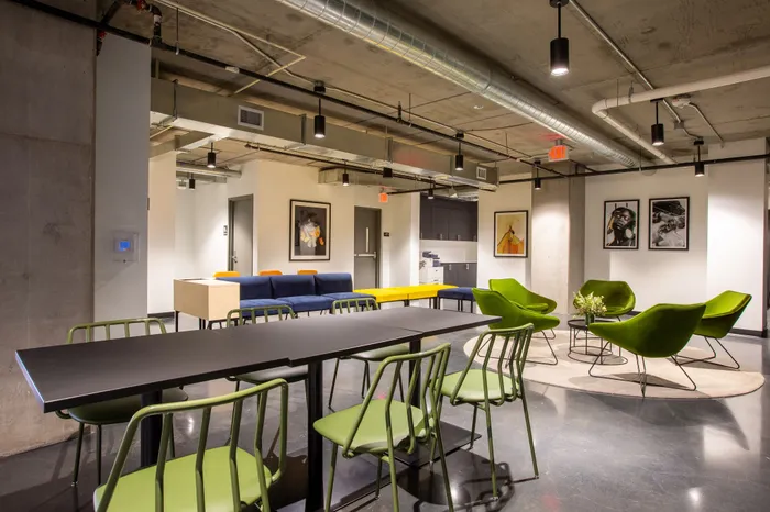 Modern communal lounge with vibrant green chairs, sleek black table, and contemporary art on walls, showcasing an inviting and stylish design.
