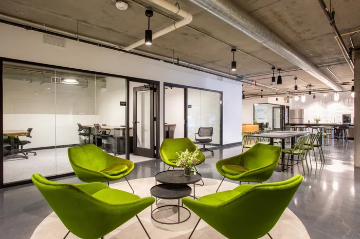 Contemporary office lounge with vibrant green chairs and sleek meeting rooms, offering a stylish and collaborative workspace.