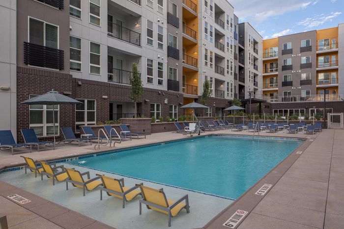 Modern apartment complex with a luxurious outdoor pool, stylish lounge chairs, and sleek urban design.