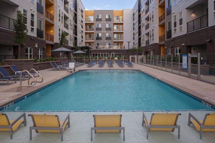 Luxurious apartment complex with a sparkling pool surrounded by stylish loungers and chic balconies, offering a vibrant urban lifestyle.