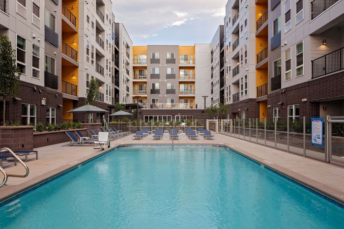 Elegant apartment complex featuring a luxurious swimming pool surrounded by comfortable lounge chairs, modern balconies, and lush greenery.