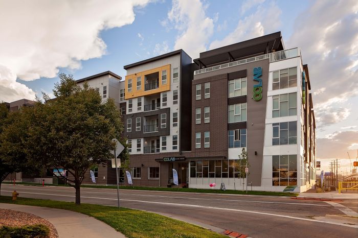 Contemporary apartment building with modern architecture and spacious balconies, set against a vibrant sunset sky.