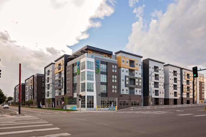Modern urban apartment complex featuring sleek architecture with large windows and vibrant accents, perfectly situated at a corner for convenience.