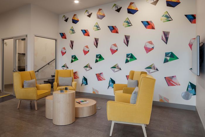 Modern lounge area with vibrant yellow chairs and a colorful geometric art wall, creating a lively and inviting atmosphere.