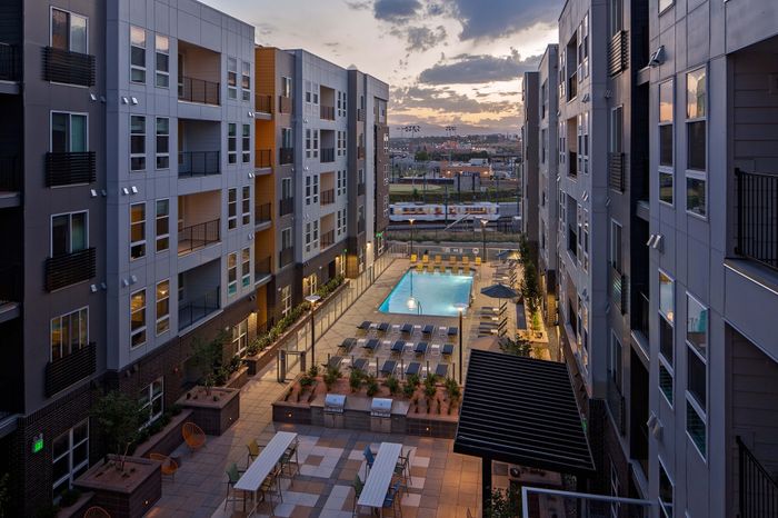 Contemporary urban apartment complex with a vibrant courtyard featuring a sparkling pool and stylish lounging areas at sunset.