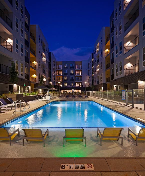 Luxurious apartment complex with a beautifully lit pool area and stylish outdoor seating, ideal for evening relaxation.