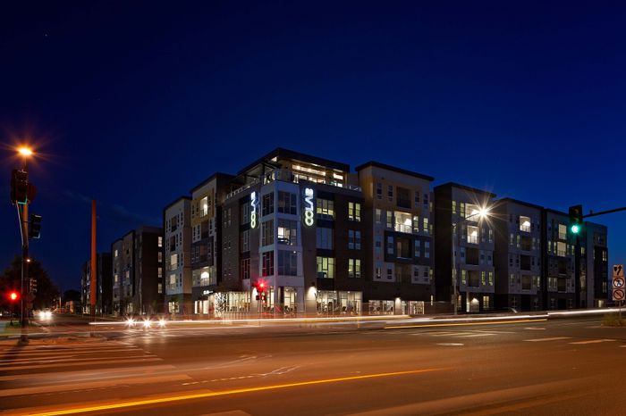 Modern apartment complex brilliantly illuminated at night, showcasing sleek architecture and urban living in a vibrant city setting.