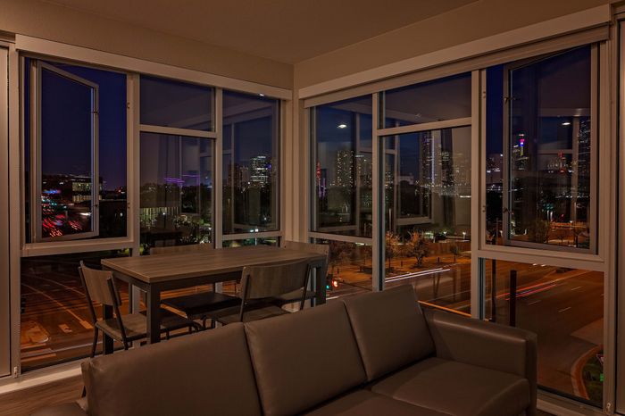 Luxurious apartment interior featuring modern furnishings with expansive windows showcasing a stunning city skyline at night.