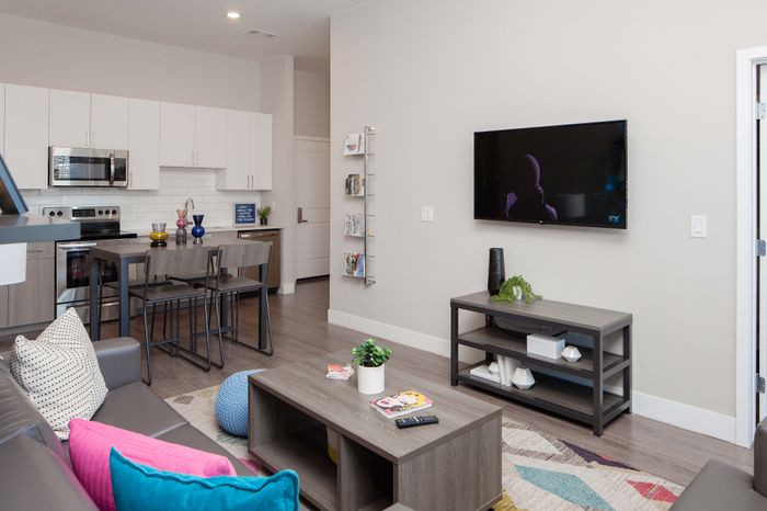 Modern open-concept living area with sleek kitchen, cozy seating, vibrant accents, and wall-mounted TV.