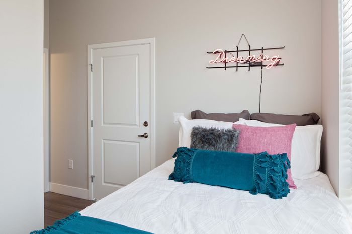 Cozy bedroom with chic decor, featuring a stylish neon sign above a plush bed adorned with colorful pillows.