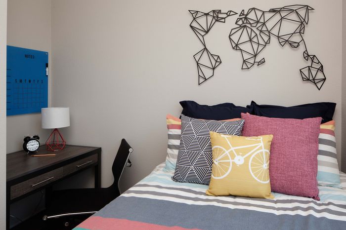 Cozy bedroom with a modern desk and geometric world map wall art, featuring colorful pillows and an inviting atmosphere.
