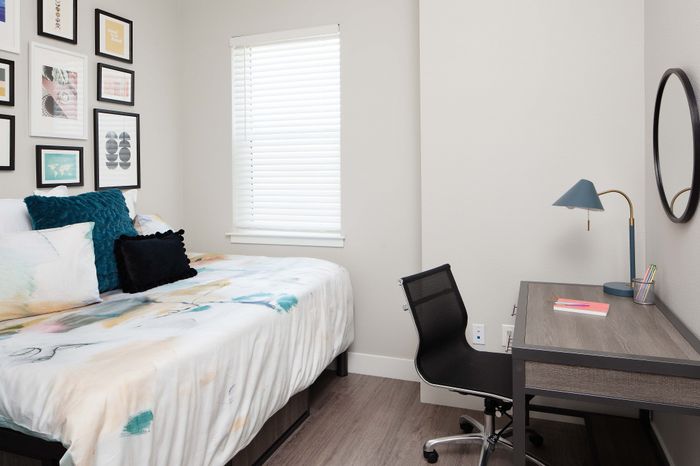 Cozy modern bedroom with stylish decor, featuring a comfortable bed, vibrant artwork, and a sleek workspace with a chic lamp.
