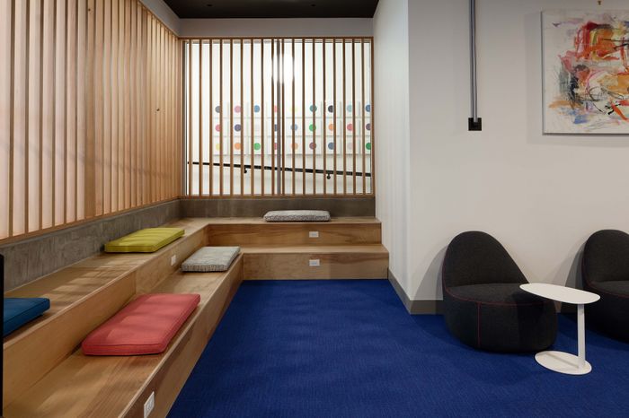 Modern seating area with colorful cushions on wooden steps, paired with chic black chairs and a minimalist white table on vibrant blue carpet.