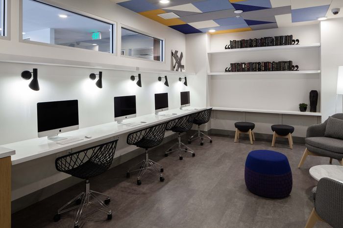 Modern co-working space with sleek white desks, high-end computers, stylish black chairs, and contemporary decor.