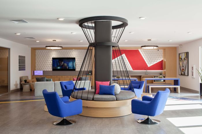 Contemporary lounge area with vibrant blue chairs, modern artwork, and sleek decor, accented by unique geometric design elements and a stylish central seating structure.