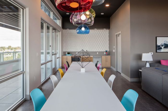 Modern dining area with colorful chairs and large windows offering natural light and scenic views, featuring sleek decor and an open-concept design.