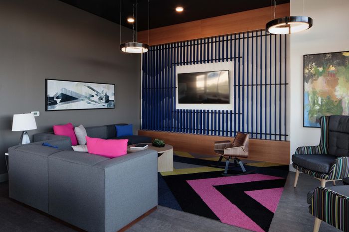 Modern living room with stylish gray sectional sofa, vibrant pink and blue cushions, geometric art pieces, and contemporary lighting.