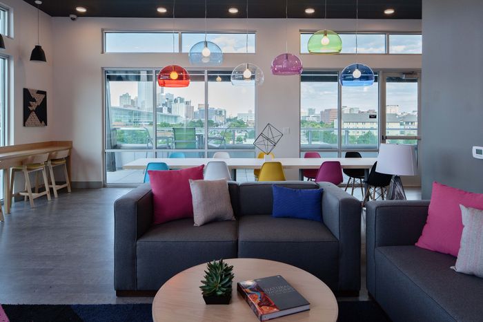 Vibrant and modern lounge area featuring colorful pendant lights, cozy seating with bold cushions, and expansive city views through large windows.