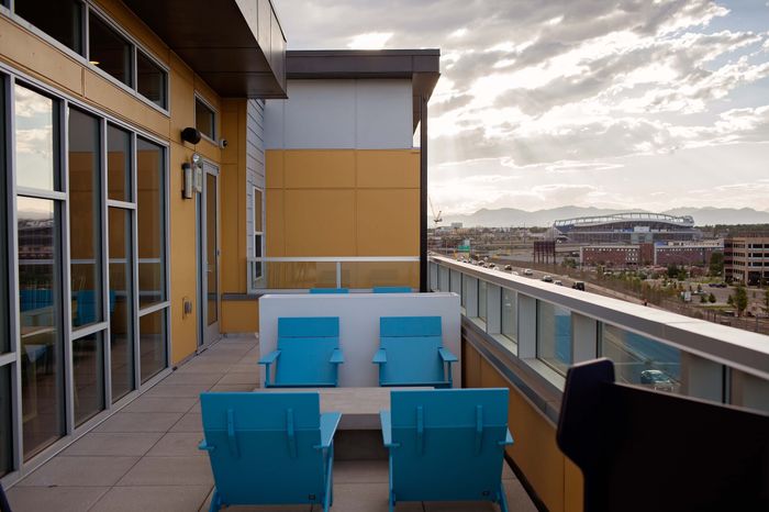 Chic urban terrace with vibrant blue seating, overlooking a bustling cityscape and mountains at sunset.