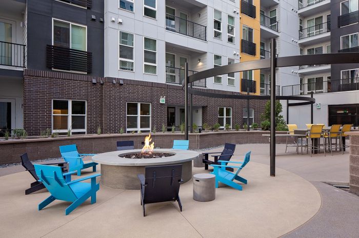 Chic urban terrace with vibrant blue seating, overlooking a bustling cityscape and mountains at sunset.