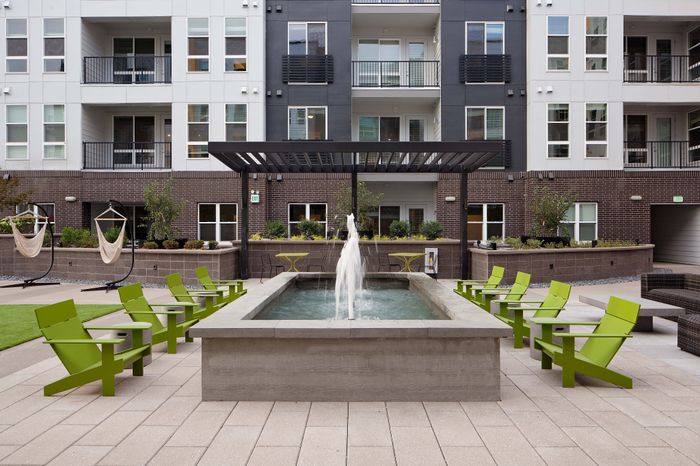 Contemporary apartment courtyard with a central fountain surrounded by modern green chairs and elegant hammocks.