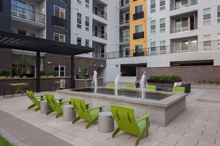 Modern apartment courtyard featuring vibrant green chairs, a sleek water fountain, and stylish outdoor seating area.