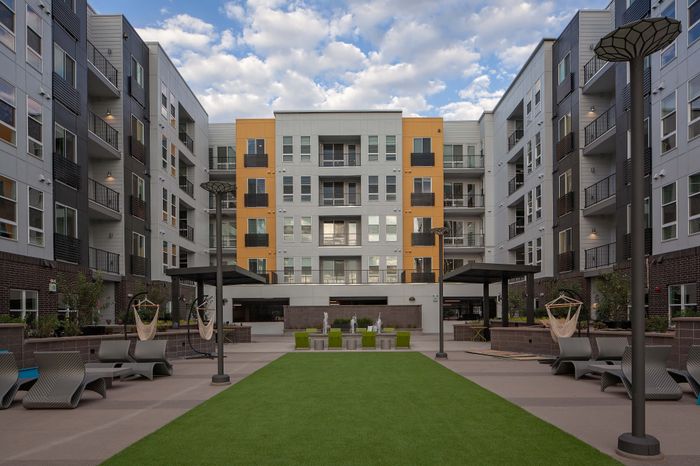 Modern apartment complex courtyard featuring lush green lawn, stylish outdoor seating, and contemporary architecture.
