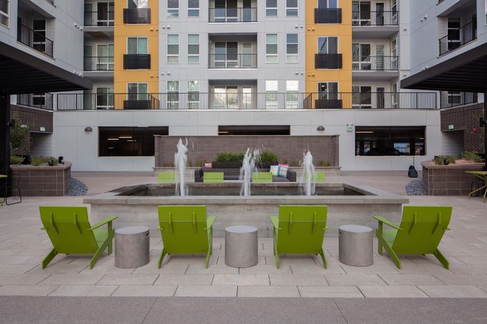 Modern apartment courtyard featuring vibrant green chairs, a stylish water fountain, and a striking yellow accent wall, offering a perfect relaxation spot.