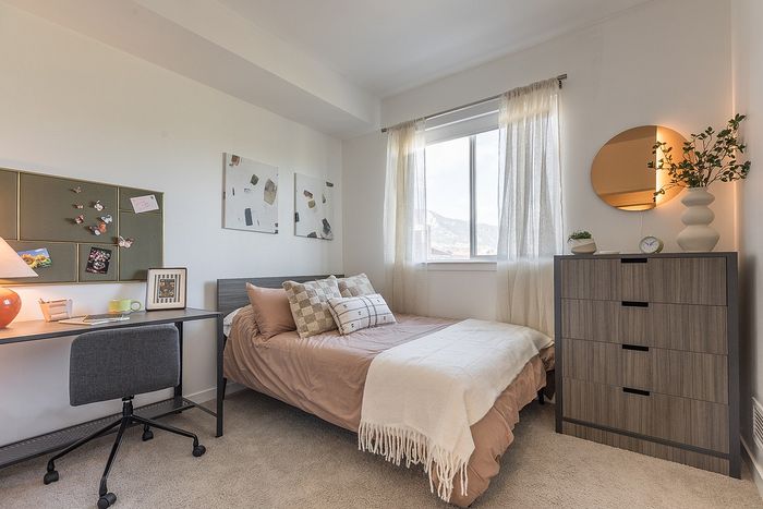 Charming bedroom with a warm ambiance, featuring a cozy bed, modern dresser, and a scenic window view.