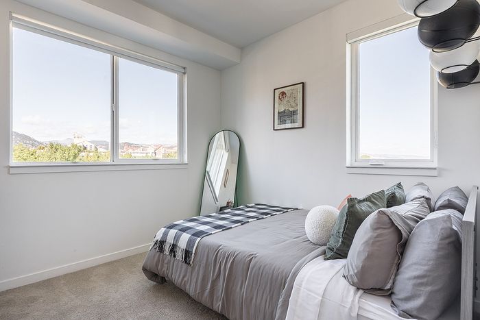 Bright bedroom with large windows, cozy bed with stylish pillows, and a chic standing mirror, offering serene views.