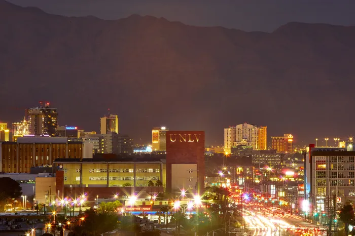 Vibrant nighttime cityscape of Las Vegas featuring illuminated urban buildings and bustling streets with the mountains in the background.