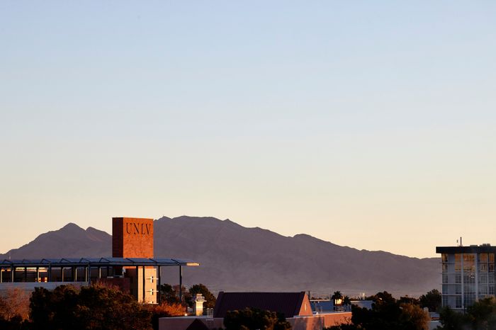 Scenic view of a university building with a backdrop of majestic mountains during sunset.