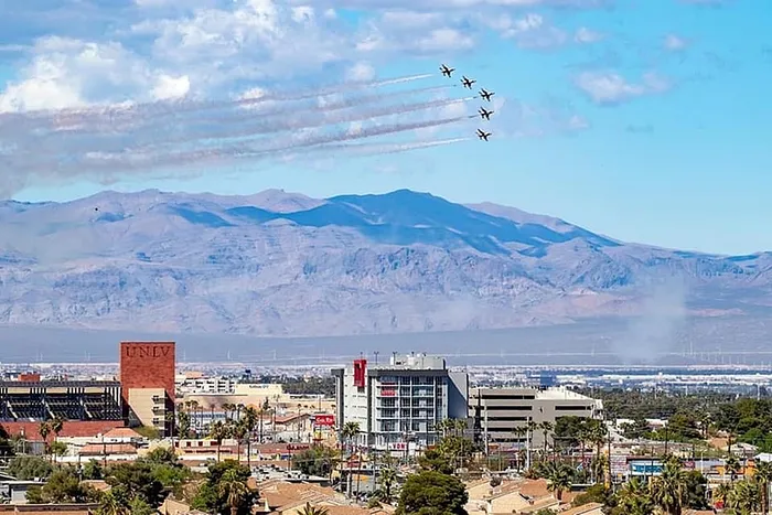 Breathtaking aerial view of a vibrant cityscape against majestic mountains, highlighted by jets soaring in formation under a clear blue sky.