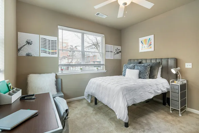 Bright and modern bedroom with plush decor, featuring cozy bedding, stylish artwork, and ample natural light from large windows. Perfect for a serene and relaxing atmosphere.