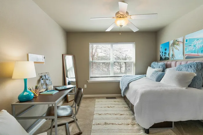 Inviting bedroom with a chic workspace, cozy bed, and vibrant decor under soft natural light.