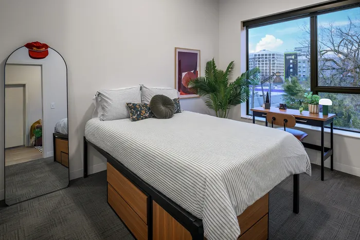 Chic bedroom with a cozy bed, modern decor, and a large window offering a picturesque urban view, perfect for city living.