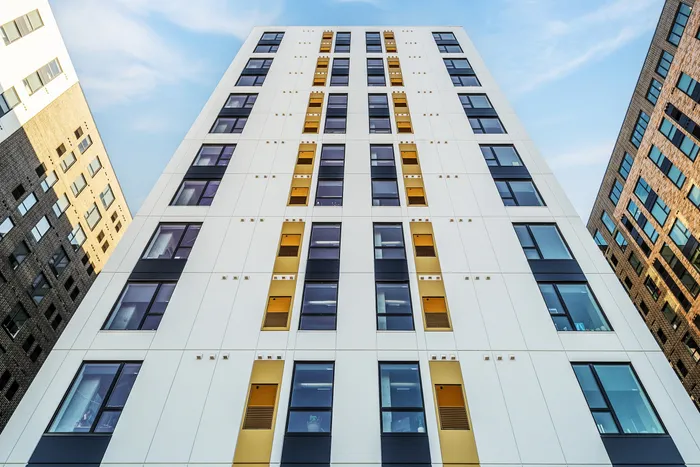 Modern high-rise apartment building with sleek white facade, large windows, and eye-catching gold accents under a clear blue sky, offering urban living at its finest.