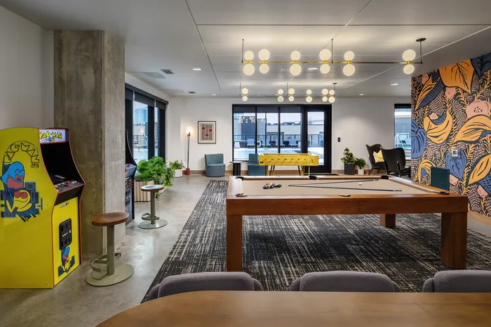 Vibrant recreational room featuring a classic Pac-Man arcade game, a sleek pool table, and a colorful foosball table, enhanced by modern decor and playful wall art.